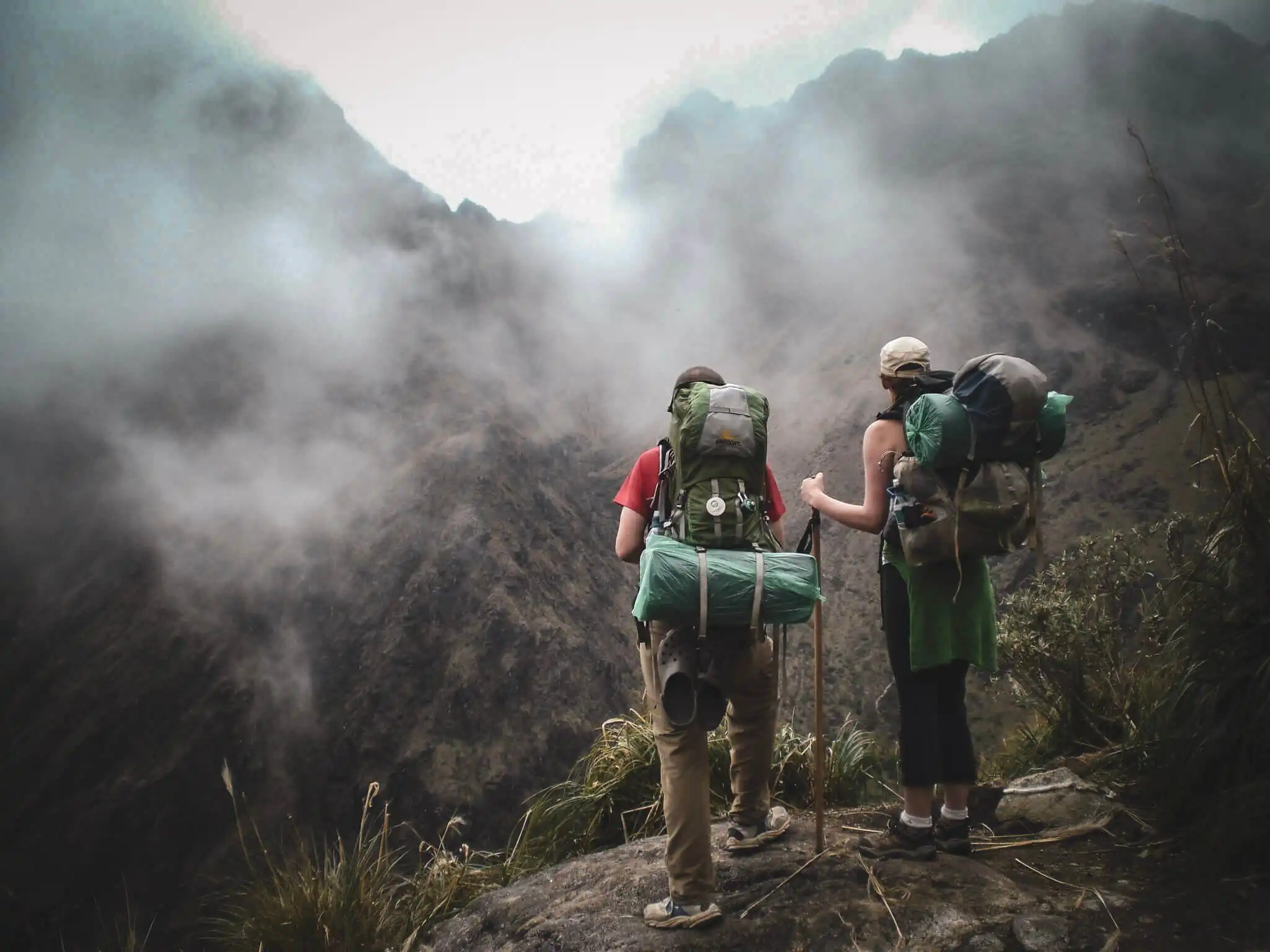 Hikers with trekking poles and loaded backpacks crossing steep, misty Inca Trail terrain