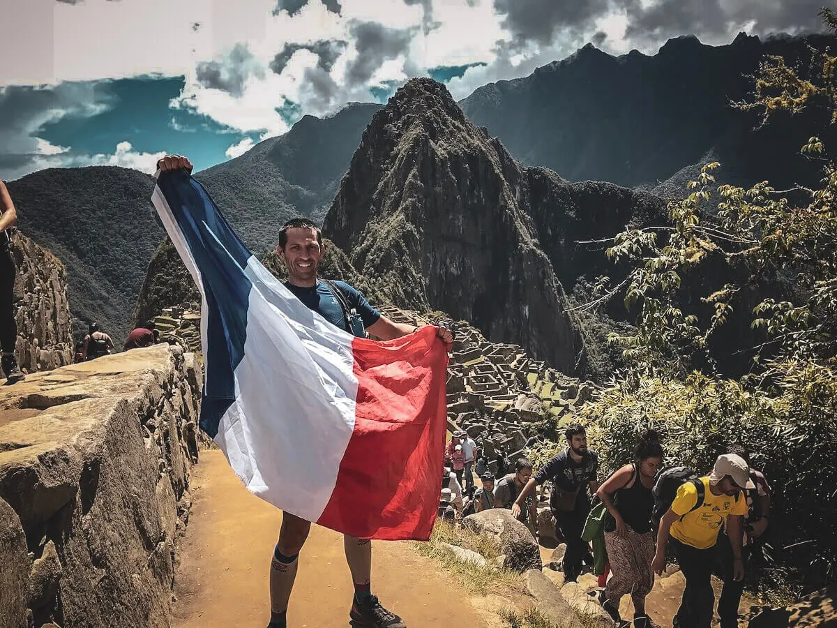 Corredor con una bandera francesa sobre Machu Picchu durante un viaje de evento anterior